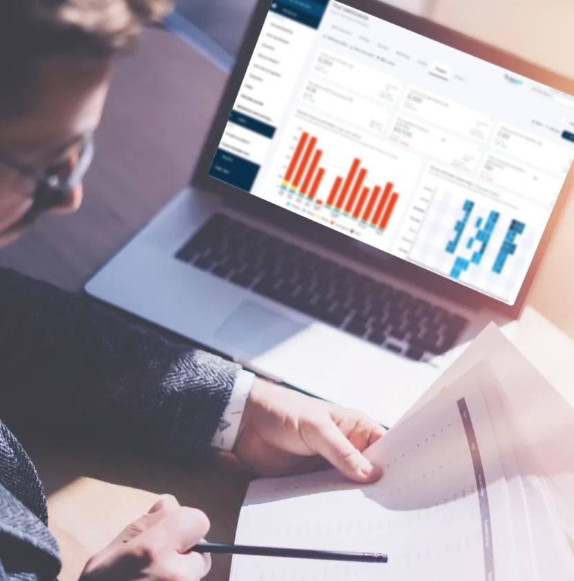 Person reviewing printed reports while analyzing FitnessKPI dashboard with charts on a laptop screen.