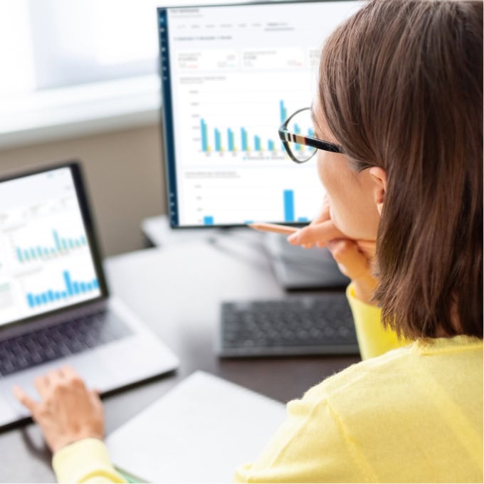Person analyzing FitnessKPI dashboards with charts on a laptop and a large monitor at a desk.