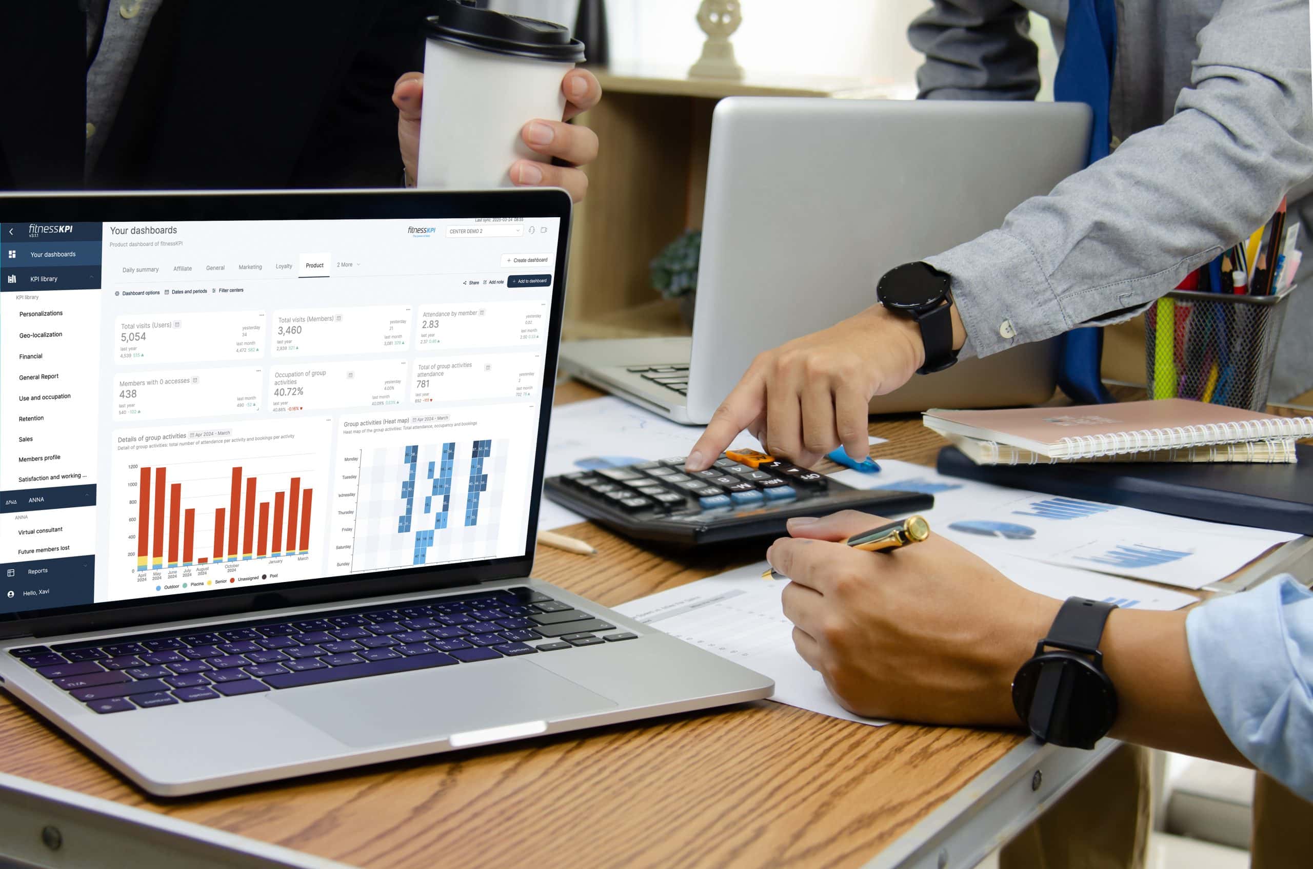 Team analyzing FitnessKPI dashboard on a laptop with charts and KPIs, while calculating data with documents on the desk.