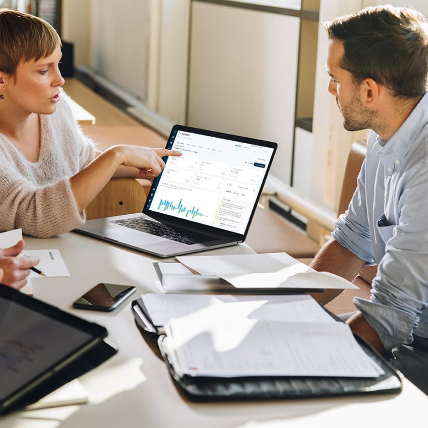 Two people in a meeting reviewing FitnessKPI dashboard data on a laptop, with documents and devices on the table.